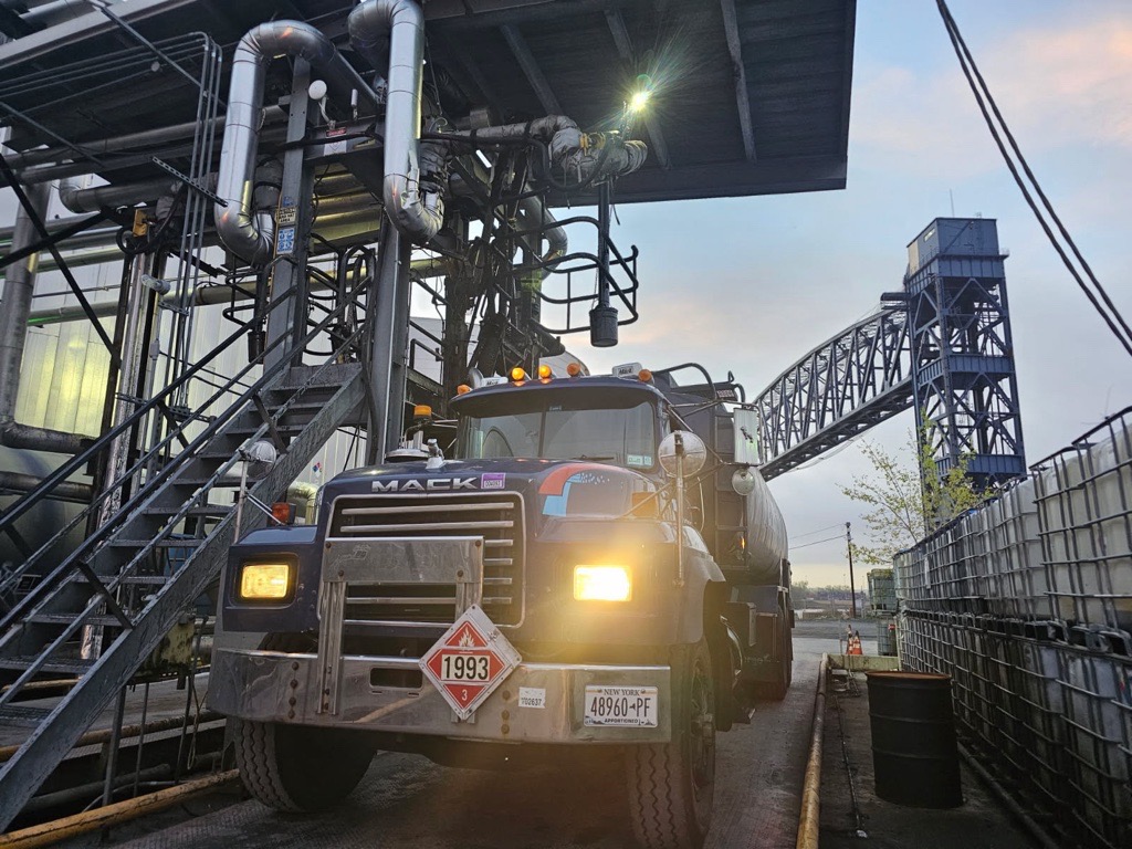 Energo oil truck operating at industrial site under overhead pipes